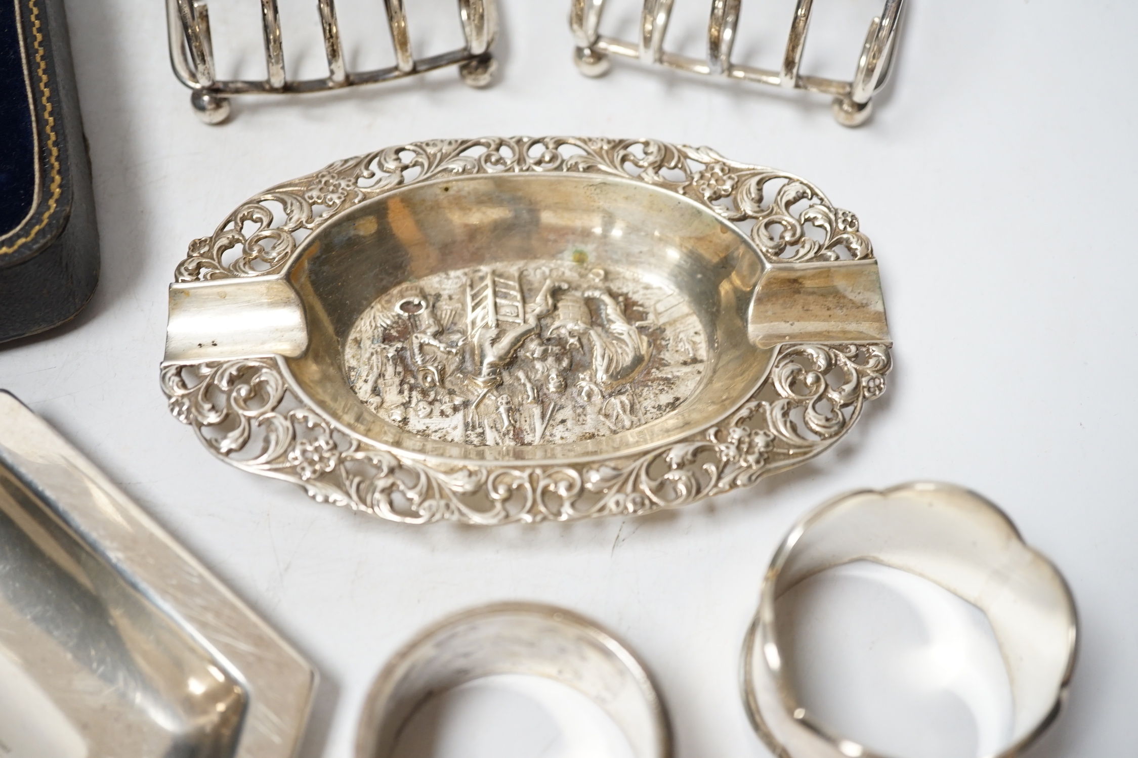 A Dutch white metal ashtray, with pierced border, 13.1cm and one other silver hexagonal ashtray?, a pair of small silver toastracks, two silver napkin rings and six items of silver flatware, including pair of Irish condi